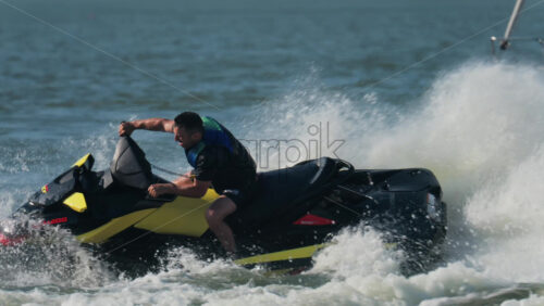 Chisinau, Moldova – June 17, 2025: A man in a black life vest riding a black jet ski at high speed across a calm body of water - Starpik Stock