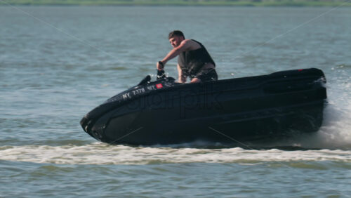 Chisinau, Moldova – June 17, 2025: A man in a black life vest riding a black jet ski at high speed across a calm body of water - Starpik Stock