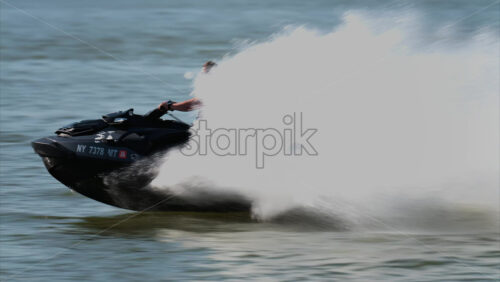 Chisinau, Moldova – June 17, 2025: A man in a black life vest riding a black jet ski at high speed across a calm body of water - Starpik Stock