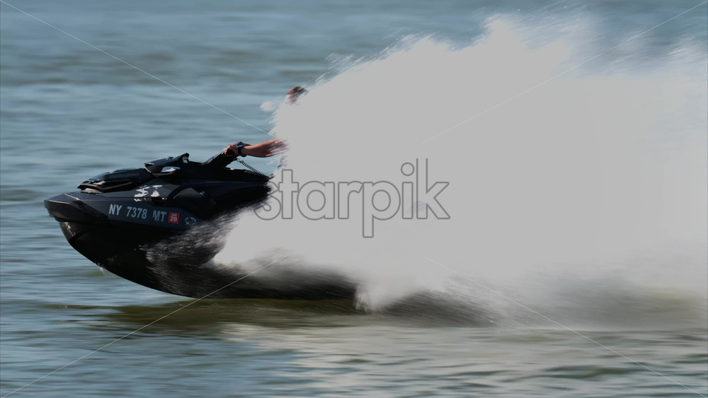 Chisinau, Moldova – June 17, 2025: A man in a black life vest riding a black jet ski at high speed across a calm body of water - Starpik Stock