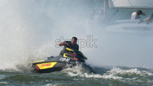 Chisinau, Moldova – June 17, 2025: A man riding a black jet ski at high speed, splashing girls on sailing trip across a calm body of water - Starpik Stock