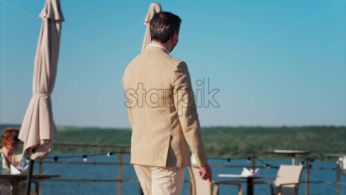 Chisinau, Moldova – June 17, 2025: Man in beige suit hopping on a scenic terrace with a view of a calm body of water - Starpik Stock
