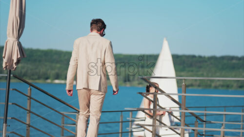 Chisinau, Moldova – June 17, 2025: Man in beige suit walking on a scenic terrace with a view of a calm body of water - Starpik Stock