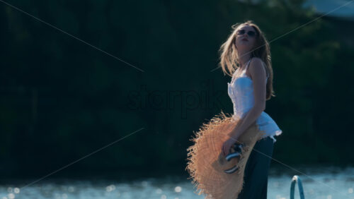 Chisinau, Moldova – June 17, 2025: Woman holding a wide-brimmed straw hat with a ribbon, soaking in the late afternoon light - Starpik Stock