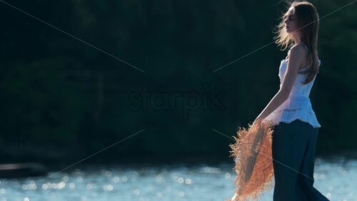 Chisinau, Moldova – June 17, 2025: Woman holding a wide-brimmed straw hat with a ribbon, soaking in the late afternoon light - Starpik Stock