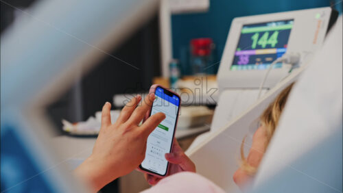 Chisinau, Moldova – May 31, 2025: Pregnant woman using the iHerb app on her phone while doing a prenatal check-up at the doctor’s office - Starpik Stock