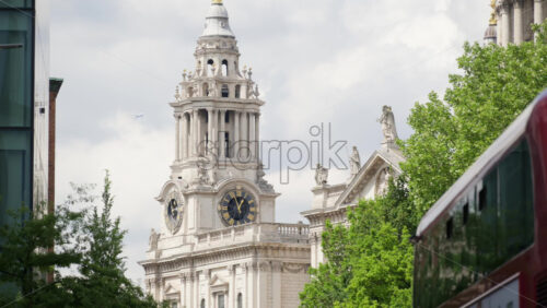 Close up of St. Paul’s Cathedral’s clock tower partially hidden by trees in London, England in daylight - Starpik Stock