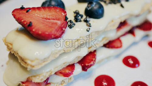 Close up of a Napoleon cake with strawberries and blueberries on a white plate at a cafe - Starpik Stock