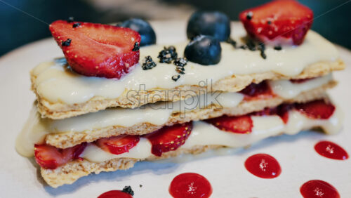 Close up of a Napoleon cake with strawberries and blueberries on a white plate at a cafe - Starpik Stock