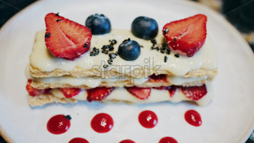 Close up of a Napoleon cake with strawberries and blueberries on a white plate at a cafe - Starpik Stock