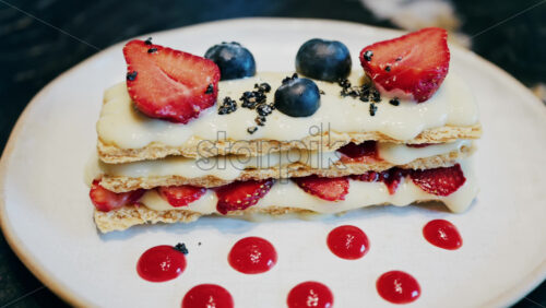 Close up of a Napoleon cake with strawberries and blueberries on a white plate at a cafe - Starpik Stock