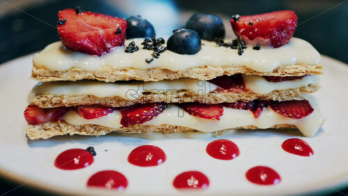 Close up of a Napoleon cake with strawberries and blueberries on a white plate at a cafe - Starpik Stock