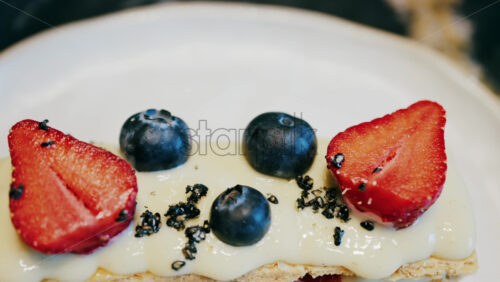 Close up of a Napoleon cake with strawberries and blueberries on a white plate at a cafe - Starpik Stock