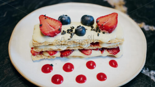 Close up of a Napoleon cake with strawberries and blueberries on a white plate at a cafe - Starpik Stock