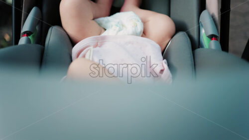 Close up of a baby wearing a pink outfit, peacefully sleeping in a stroller - Starpik Stock