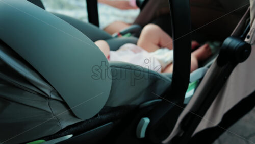 Close up of a baby wearing a pink outfit, peacefully sleeping in a stroller - Starpik Stock