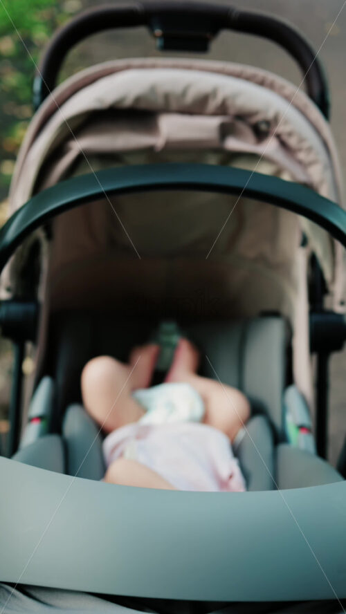 Close up of a baby wearing a pink outfit, peacefully sleeping in a stroller - Starpik Stock