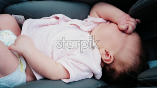 Close up of a baby wearing a pink outfit, peacefully sleeping with a hand near the face - Starpik Stock