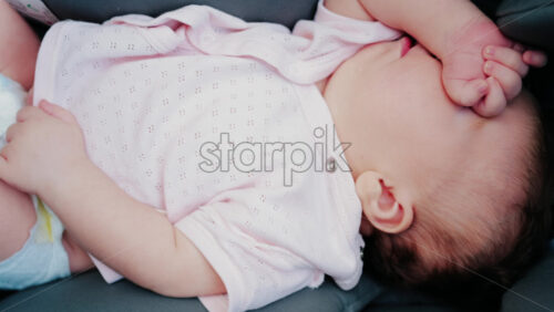 Close up of a baby wearing a pink outfit, peacefully sleeping with a hand near the face - Starpik Stock