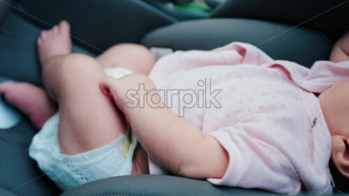 Close up of a baby wearing a pink outfit, peacefully sleeping with a hand near the face - Starpik Stock