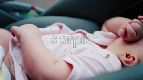 Close up of a baby wearing a pink outfit, peacefully sleeping with a hand near the face - Starpik Stock