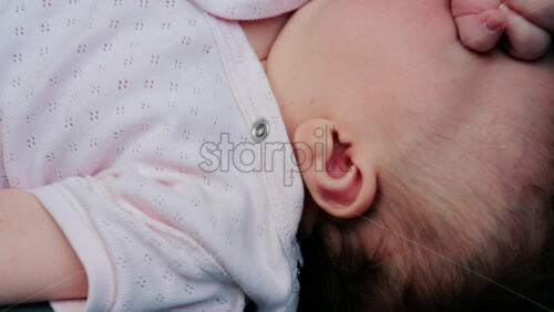 Close up of a baby wearing a pink outfit, peacefully sleeping with a hand near the face - Starpik Stock