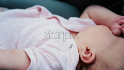 Close up of a baby wearing a pink outfit, peacefully sleeping with a hand near the face - Starpik Stock