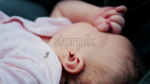 Close up of a baby wearing a pink outfit, peacefully sleeping with a hand near the face - Starpik Stock
