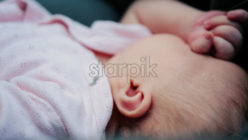 Close up of a baby wearing a pink outfit, peacefully sleeping with a hand near the face - Starpik Stock