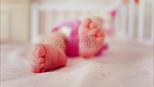 Close up of a baby’s feet resting in a crib while wearing a pink outfit - Starpik Stock