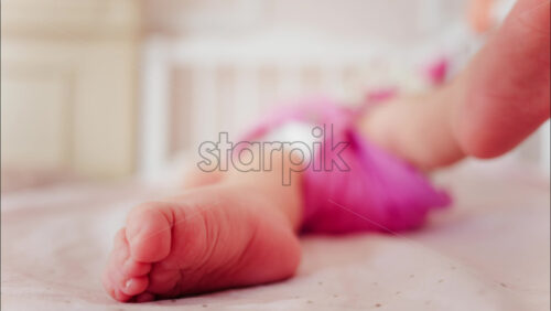 Close up of a baby’s feet resting in a crib while wearing a pink outfit - Starpik Stock