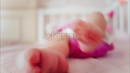 Close up of a baby’s feet resting in a crib while wearing a pink outfit - Starpik Stock