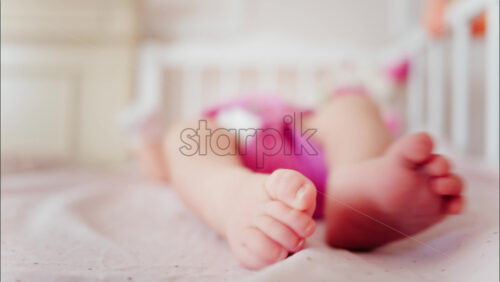 Close up of a baby’s feet resting in a crib while wearing a pink outfit - Starpik Stock
