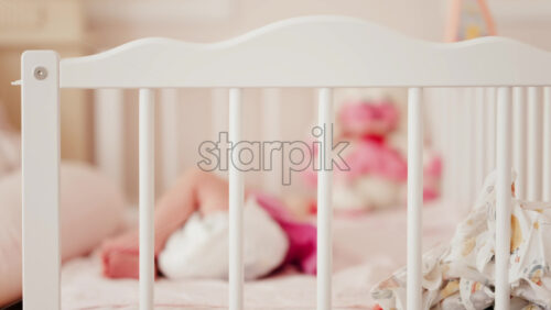 Close up of a baby’s legs and diaper as the infant rests in a crib, seen through the crib bars - Starpik Stock