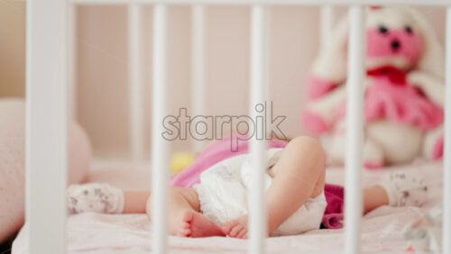Close up of a baby’s legs and diaper as the infant rests in a crib, seen through the crib bars - Starpik Stock