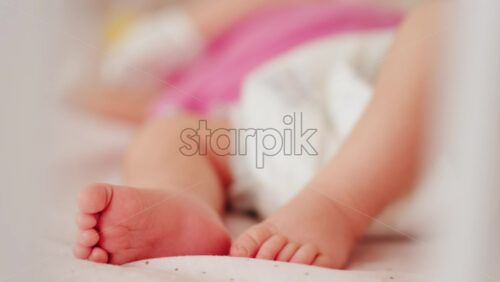 Close up of a baby’s legs and diaper as the infant rests in a crib, seen through the crib bars - Starpik Stock