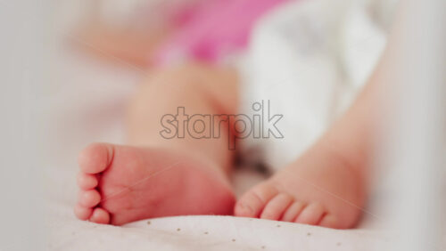 Close up of a baby’s legs and diaper as the infant rests in a crib, seen through the crib bars - Starpik Stock