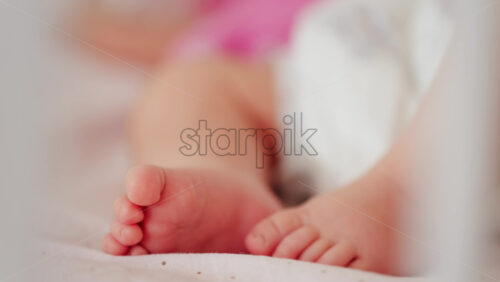 Close up of a baby’s legs and diaper as the infant rests in a crib, seen through the crib bars - Starpik Stock