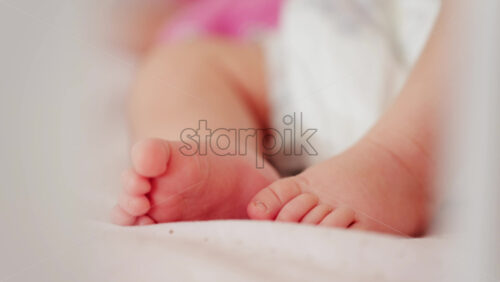 Close up of a baby’s legs and diaper as the infant rests in a crib, seen through the crib bars - Starpik Stock
