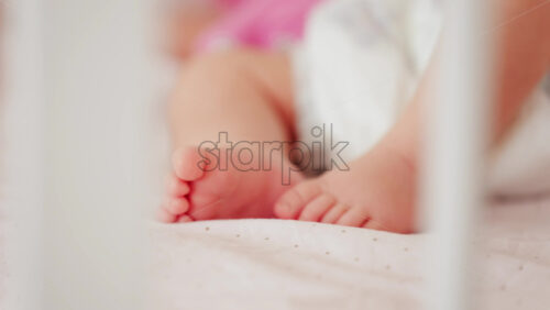 Close up of a baby’s legs and diaper as the infant rests in a crib, seen through the crib bars - Starpik Stock