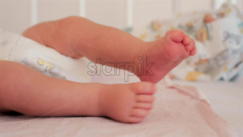 Close up of a baby’s legs and diaper as the infant rests in a crib, seen through the crib bars - Starpik Stock