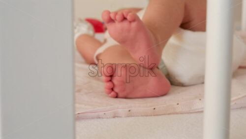 Close up of a baby’s legs and diaper as the infant rests in a crib, seen through the crib bars - Starpik Stock