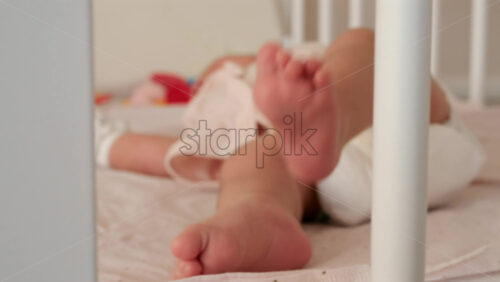 Close up of a baby’s legs and diaper as the infant rests in a crib, seen through the crib bars - Starpik Stock