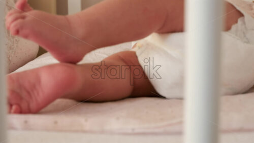Close up of a baby’s legs and diaper as the infant rests in a crib, seen through the crib bars - Starpik Stock