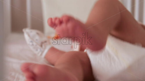 Close up of a baby’s legs and diaper as the infant rests in a crib, seen through the crib bars - Starpik Stock