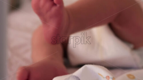 Close up of a baby’s legs and diaper as the infant rests in a crib, seen through the crib bars - Starpik Stock