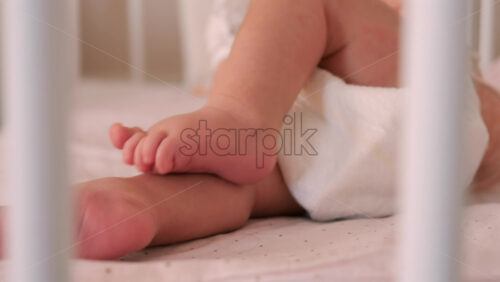 Close up of a baby’s legs and diaper as the infant rests in a crib, seen through the crib bars - Starpik Stock