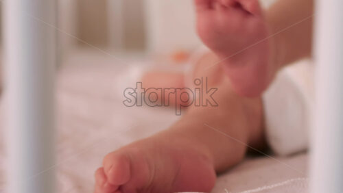 Close up of a baby’s legs and diaper as the infant rests in a crib, seen through the crib bars - Starpik Stock