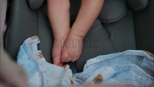 Close up of a baby’s small feet moving near a patterned blanket inside a car seat - Starpik Stock