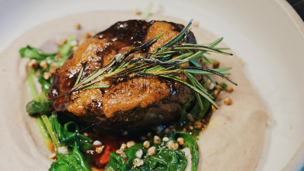 Close up of a beautifully plated beef filet, topped with a golden crust and garnished with rosemary - Starpik Stock